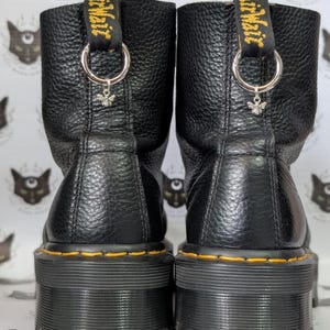 May include: Black leather platform boots with yellow stitching and a black and yellow "Dr. Martens" tag on the back of each boot. The boots have a silver charm attached to a silver ring on the back of each boot.