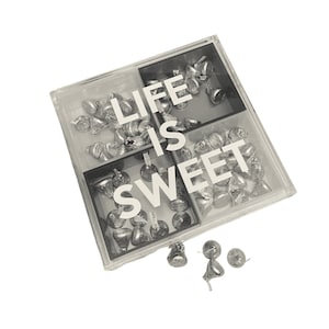 May include: A clear plastic box with four compartments filled with silver foil-wrapped chocolates. The box has the text "LIFE IS SWEET" printed on the front.