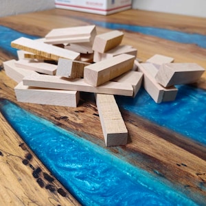 May include: A pile of unfinished wooden blocks in various sizes and shapes, arranged on a blue and brown epoxy resin table.