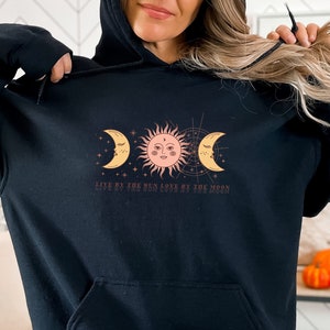 May include: Black hooded sweatshirt with a graphic of a sun and two moons with the text "Live by the sun love by the moon".