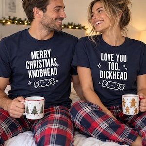 May include: Two navy blue short-sleeved t-shirts featuring white text and graphics. One shirt reads MERRY CHRISTMAS, KNOBHEAD with a candy graphic. The other reads LOVE YOU TOO, DICKHEAD with a candy graphic. Both shirts are worn with red and blue plaid pants.