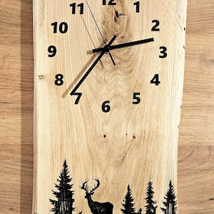 May include: A wooden clock with black hands and black numbers on a light brown wood background. The clock has a deer and trees silhouetted below the clock face.