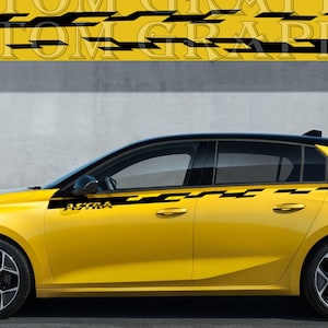 May include: A yellow car with black accents and black wheels. The car has black and yellow graphics that say "ASTRA" and "CUSTOM GRAPHICS". The car is parked in front of a gray wall.