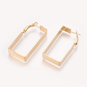 May include: A pair of gold-toned hoop earrings featuring a rectangular shape with a smooth, flat surface. Each earring is constructed from a continuous metal band that forms an open rectangle, secured with a hinged post closure at the top corner.