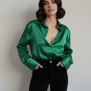 Könnte beinhalten: Ein leuchtend grünes Seidenhemd mit Knopfleiste und langen Ärmeln. Das Hemd wird mit einer schwarzen Cordhose kombiniert. Eine goldene Halskette ist sichtbar. Der Look ist stilvoll und elegant.