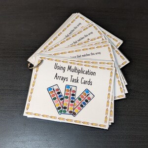 May include: A set of task cards for teaching multiplication using arrays. The cards feature a colorful watercolor paint set with a paintbrush. The text on the cards reads "Using Multiplication Arrays Task Cards".