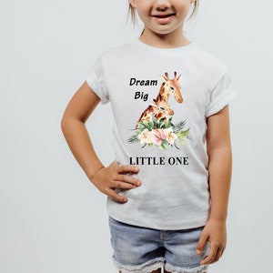 May include: White t-shirt with a watercolor illustration of a mother and baby giraffe surrounded by flowers. The text "Dream Big Little One" is printed below the image.