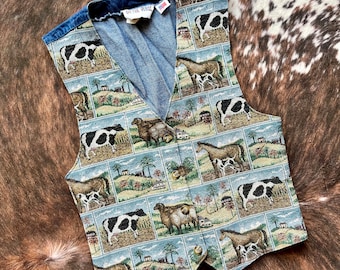 May include: A blue denim vest with a tapestry pattern featuring farm animals, including cows, sheep, and horses. The vest has a V-neck and a button closure. The text "On The Farm" is visible on the inside of the vest.