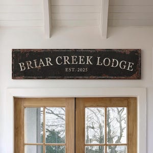 May include: A rustic black sign with white text that reads "Briar Creek Lodge Est. 2025". The sign is made to look like weathered metal.