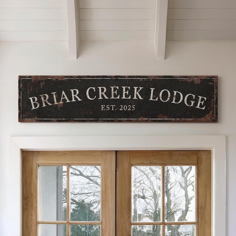 May include: A rustic black sign with white text that reads "Briar Creek Lodge Est. 2025". The sign is made to look like weathered metal.