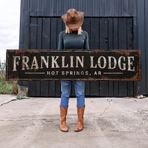 May include: A rustic black metal sign with white lettering that reads "FRANKLIN LODGE - HOT SPRINGS, AR".