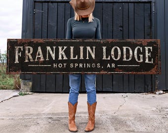 May include: A rustic black metal sign with white lettering that reads "FRANKLIN LODGE - HOT SPRINGS, AR".