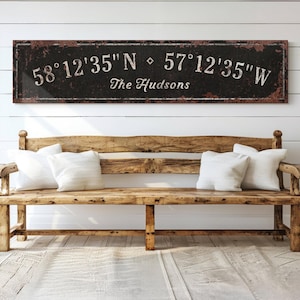 May include: A black and brown rustic wooden sign with white text. The sign reads "58°12'35"N  57°12'35"W The Hudsons".