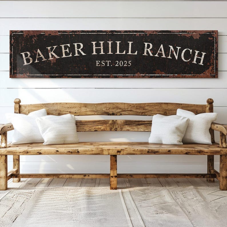 May include: A rustic wooden sign with black background and white lettering that reads "Baker Hill Ranch Est. 2025". The sign is hanging on a white shiplap wall above a wooden bench.