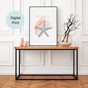 Peut inclure: Impression numérique encadrée avec une étoile de mer bleue à l'aquarelle sur fond pêche. Les mots "étoile de mer" sont écrits au-dessus. L'impression est posée sur une table en bois avec des pieds en métal noir, avec des vases et un vase en verre avec des branches.