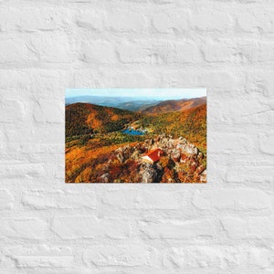 Può includere: Una vista aerea di una piccola capanna con un tetto rosso incastonata in un paesaggio montano. Gli alberi circostanti sono un mix di verde e arancione, a indicare l'autunno. Un piccolo lago è visibile in lontananza.