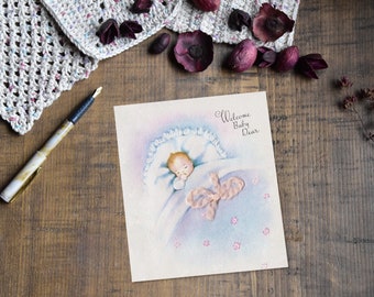 May include: A vintage baby card with a pastel blue and pink color scheme. The card features a baby sleeping in a crib with a pink butterfly. The text on the card reads "Welcome Baby Dear".