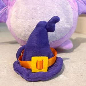 May include: A purple and blue witch hat with an orange ribbon and a yellow buckle. The hat is made of soft fabric and has a pointed top.