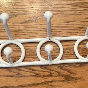 May include: White plastic coat rack with six hooks. The rack is designed with a series of connected circles, each with a hook extending upwards.