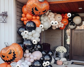 May include: A Halloween-themed balloon arch featuring orange and black balloons, with large pumpkin-shaped balloons and white balloons with googly eyes. The arch is decorated with bats and is set up on a porch.