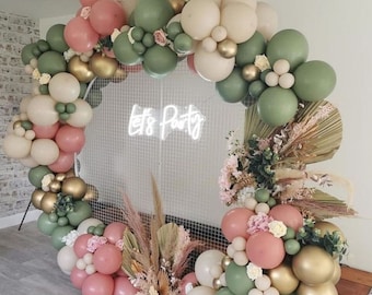 May include: A balloon arch made of green, beige, and pink balloons with the words "Let's Party" in neon lights. The arch is decorated with dried grasses and greenery.