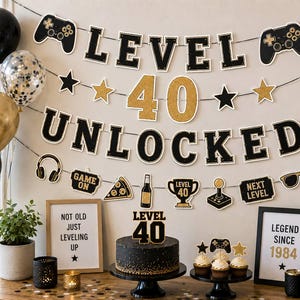 May include: A birthday party decoration set featuring a black and gold banner that reads LEVEL 40 UNLOCKED, with game controller, pizza, and trophy cutouts. Includes a black cake with a LEVEL 40 topper, balloons, and framed signs with text.