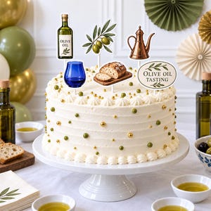 May include: A white frosted cake decorated with gold and green sprinkles, topped with six food-themed cake toppers including an olive oil bottle, green olives, a copper oil cruet, a blue glass, sliced bread, and an Olive Oil Tasting sign.