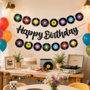 May include: A party decoration set featuring a black glittery Happy Birthday banner and two strings of vinyl record cutouts in various colors. The set includes colorful balloons, a birthday cake, and a record player on a wooden table.