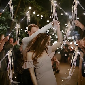 May include: A couple dances under a canopy of twinkling lights strung on white ribbons. The lights are strung on thin wires and create a magical atmosphere. The couple is smiling and enjoying the moment.