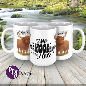 May include: White ceramic mugs featuring a Highland cow illustration with musical notes and the text "Sing Harmood Nights to the Lord." The mugs have a curved handle and a glossy finish. The mugs are on a wooden surface.