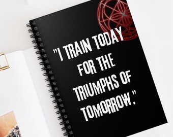 Op de afbeelding: Een zwart notitieboek met spiraalbinding, een rood geometrisch ontwerp en de quote "Ik train vandaag voor de triomfen van morgen."