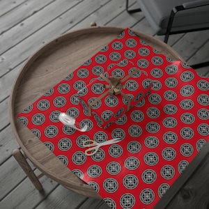 May include: A wrapped gift with a brown ribbon on red wrapping paper with a black and white circular pattern. A pair of gold scissors and a roll of white tape are on the wrapping paper.