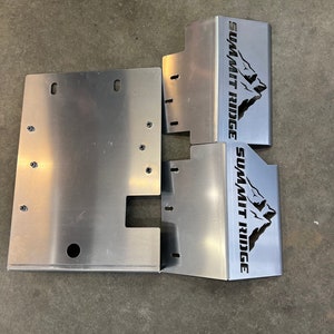 Puede incluir: Un conjunto de piezas automotrices de metal plateado. Las piezas son rectangulares y tienen varios recortes y orificios de montaje. El texto "SUMMIT RIDGE" está impreso en negro en dos de las piezas, junto con un gráfico de montaña.