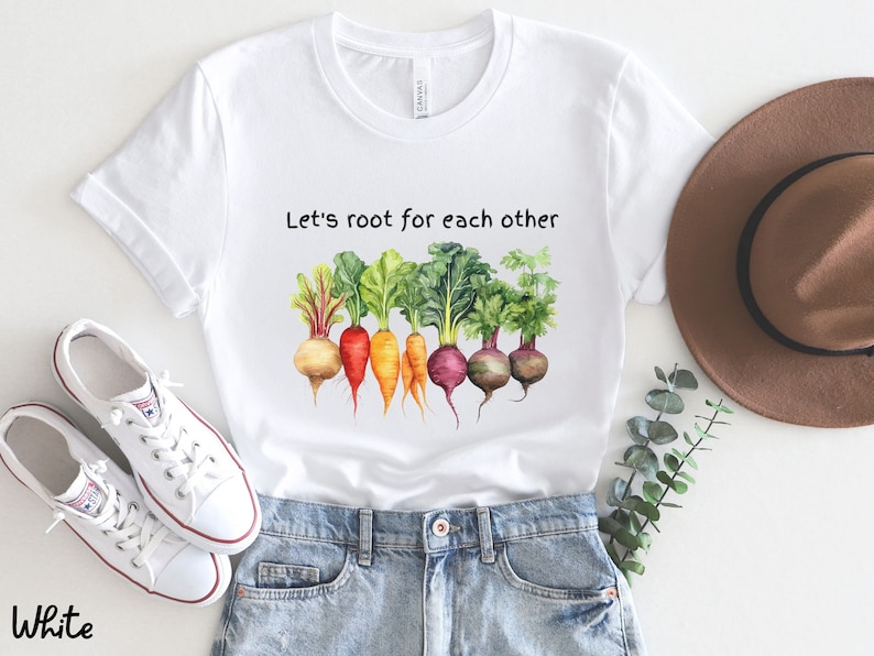 Op de afbeelding: Wit T-shirt met een aquarel-illustratie van groenten en de tekst "Let's root for each other".