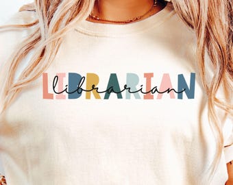 May include: Ivory-colored sweatshirt with the word "LIBRARIAN" printed across the chest in colorful block letters and a cursive font. The word is in a mix of colors: pink, blue, yellow, green, and coral. The shirt is a casual style.