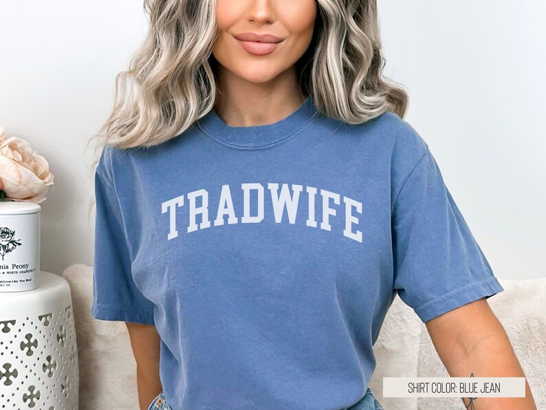 Puede incluir: Una camiseta azul jean con la palabra "TRADWIFE" impresa en blanco en la parte delantera.