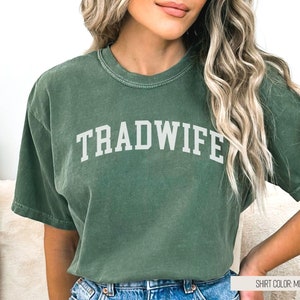 Puede incluir: Una camiseta verde con el texto "TRADWIFE" en letras blancas. El color de la camiseta es musgo.