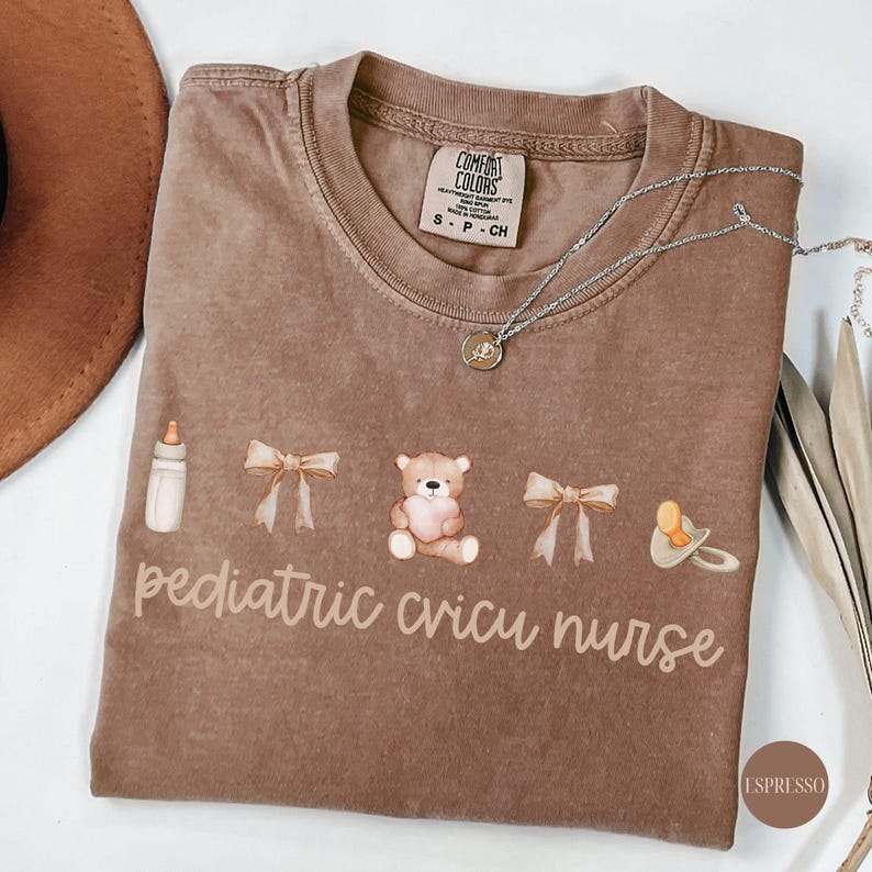 May include: A brown t-shirt with the text "pediatric cricu nurse" and illustrations of a baby bottle, a teddy bear, a bow, and a pacifier.
