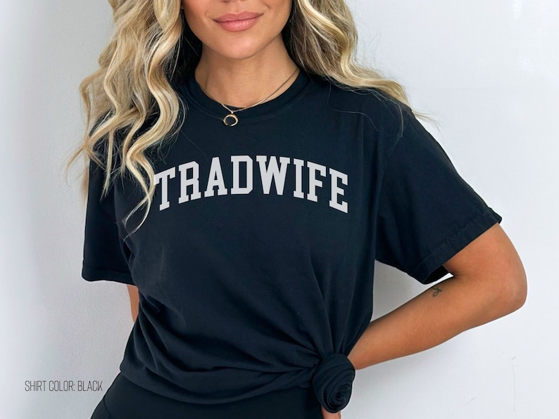 Puede incluir: Camiseta negra con el texto "TRADWIFE" en letras blancas.