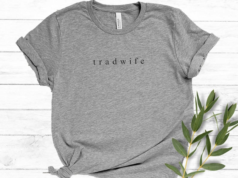 Op de afbeelding: Grijs T-shirt met de tekst "tradwife" in zwart op de voorkant.