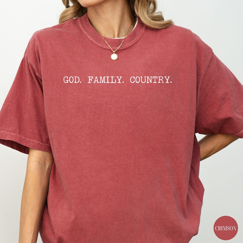 May include: Crimson-colored t-shirt with the text "GOD. FAMILY. COUNTRY." in white block letters. The shirt has short sleeves and a crew neck. The word "CRIMSON" is printed in a small circle on the bottom right.