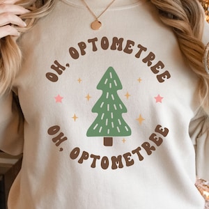 May include: A beige sweatshirt with a brown graphic of a Christmas tree and the text "Oh, Optometree" in a retro font.