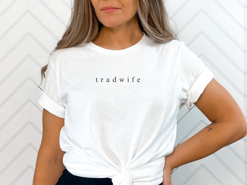 Op de afbeelding: Wit T-shirt met de tekst "trad wife" gedrukt op de voorkant.