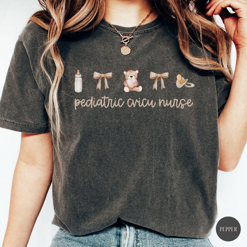May include: A dark gray t-shirt with the text "pediatric cricu nurse" and images of a baby bottle, two bows, a teddy bear, and a pacifier.