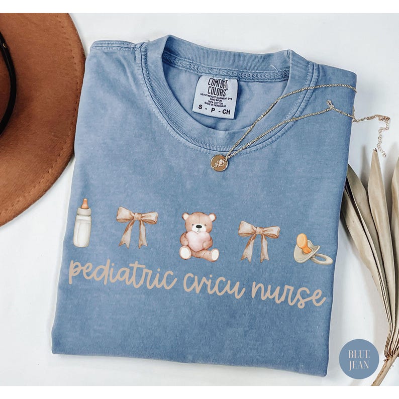 May include: A light blue t-shirt with a graphic design of a baby bottle, two bows, a teddy bear, a pacifier, and the text "pediatric cricu nurse".
