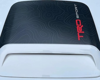 May include: A white car with a black hood scoop featuring a topographic pattern and the red text "TRD SPORT".