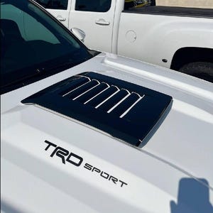 May include: White car with a black hood scoop and a black "TRD SPORT" decal on the hood.