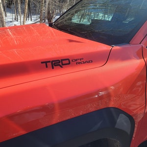 May include: A red pickup truck with a black "TRD OFF ROAD" decal on the bonnet.