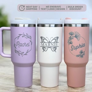 May include: Three insulated tumblers in lavender, white, and rose. Each tumbler features a personalized name in a decorative frame. The lavender tumbler has a handle. The white tumbler has a butterfly design. The rose tumbler has a floral design.