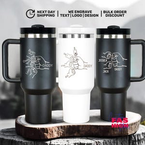 May include: Three insulated travel mugs with black handles and lids. Each mug features a personalized design with names and the word "DADDY" alongside a graphic of clasped hands. The mugs are black and white.